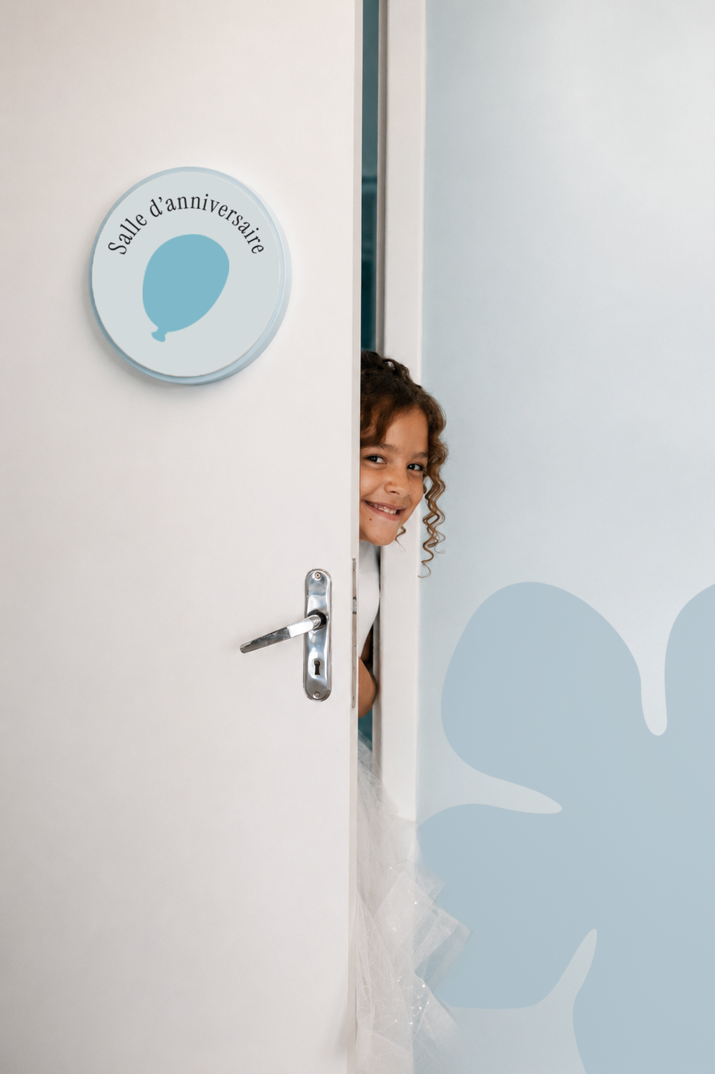 Petite fille souriante derrière la porte de la salle d'anniversaire Ludelys